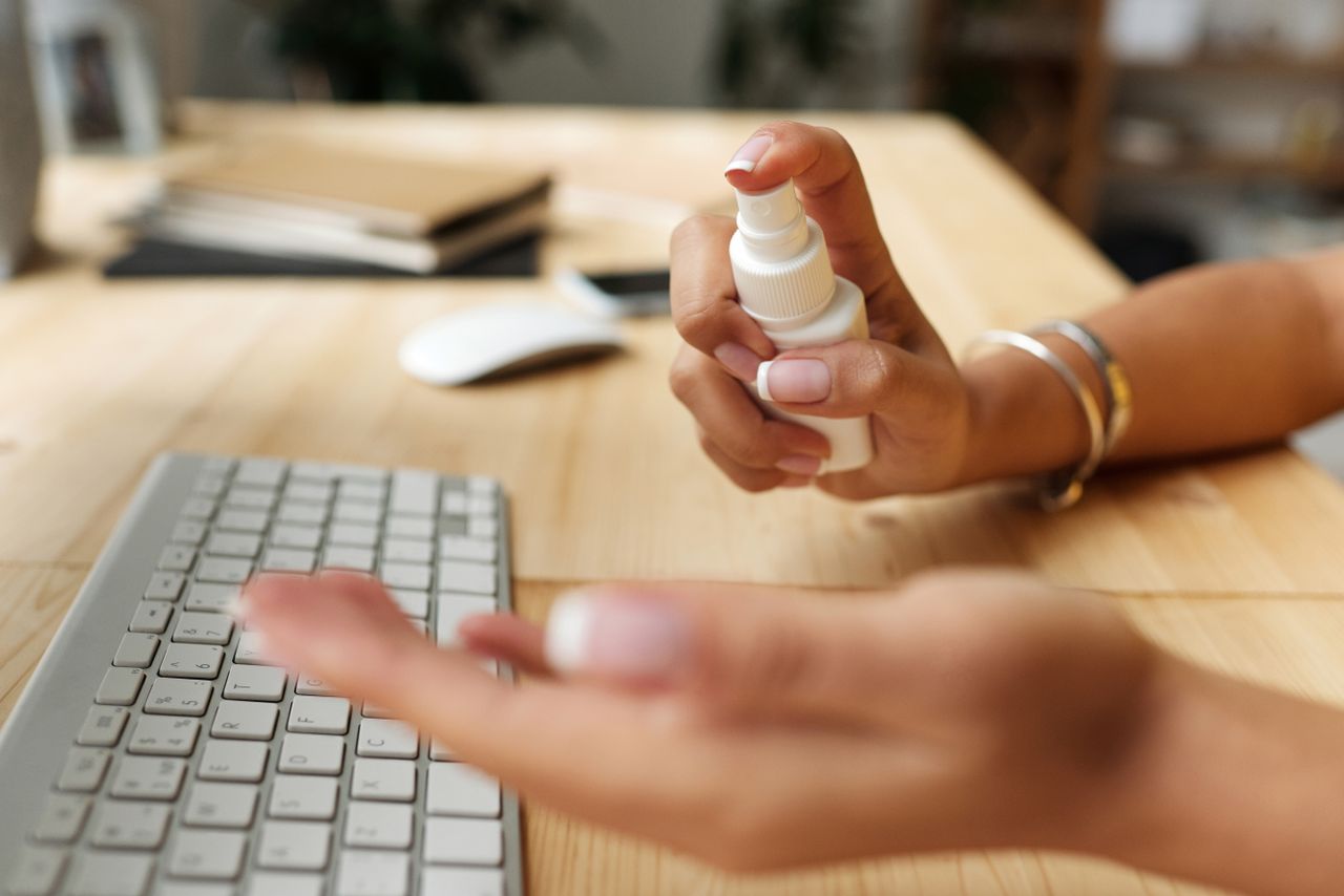 services-01 Personne se désinfectant les mains à un bureau, avec un flacon pulvérisateur, un clavier et une souris d’ordinateur.